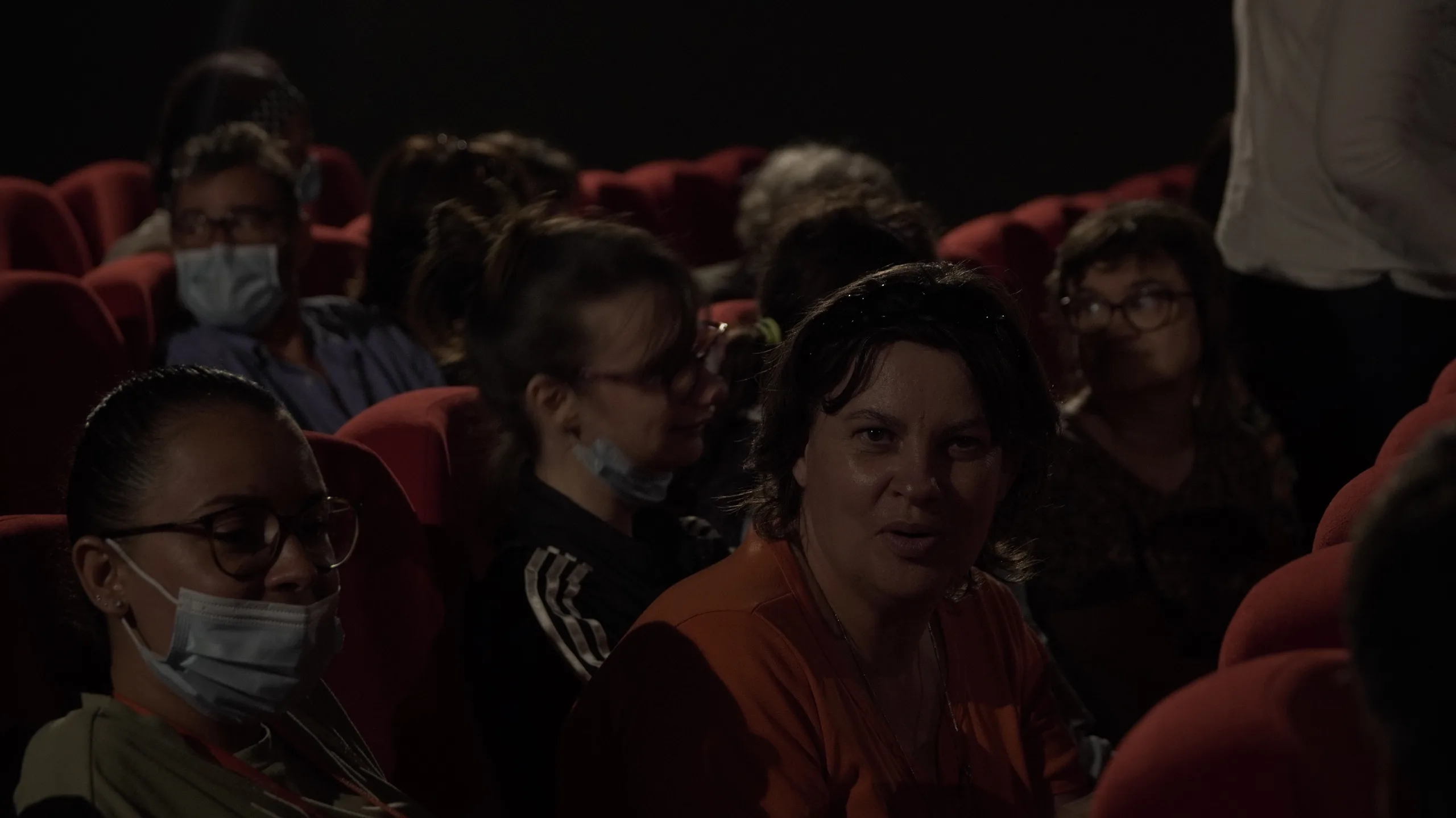 Spectateurs installés dans les fauteuils rouges d'une salle de cinéma, pendant une projection